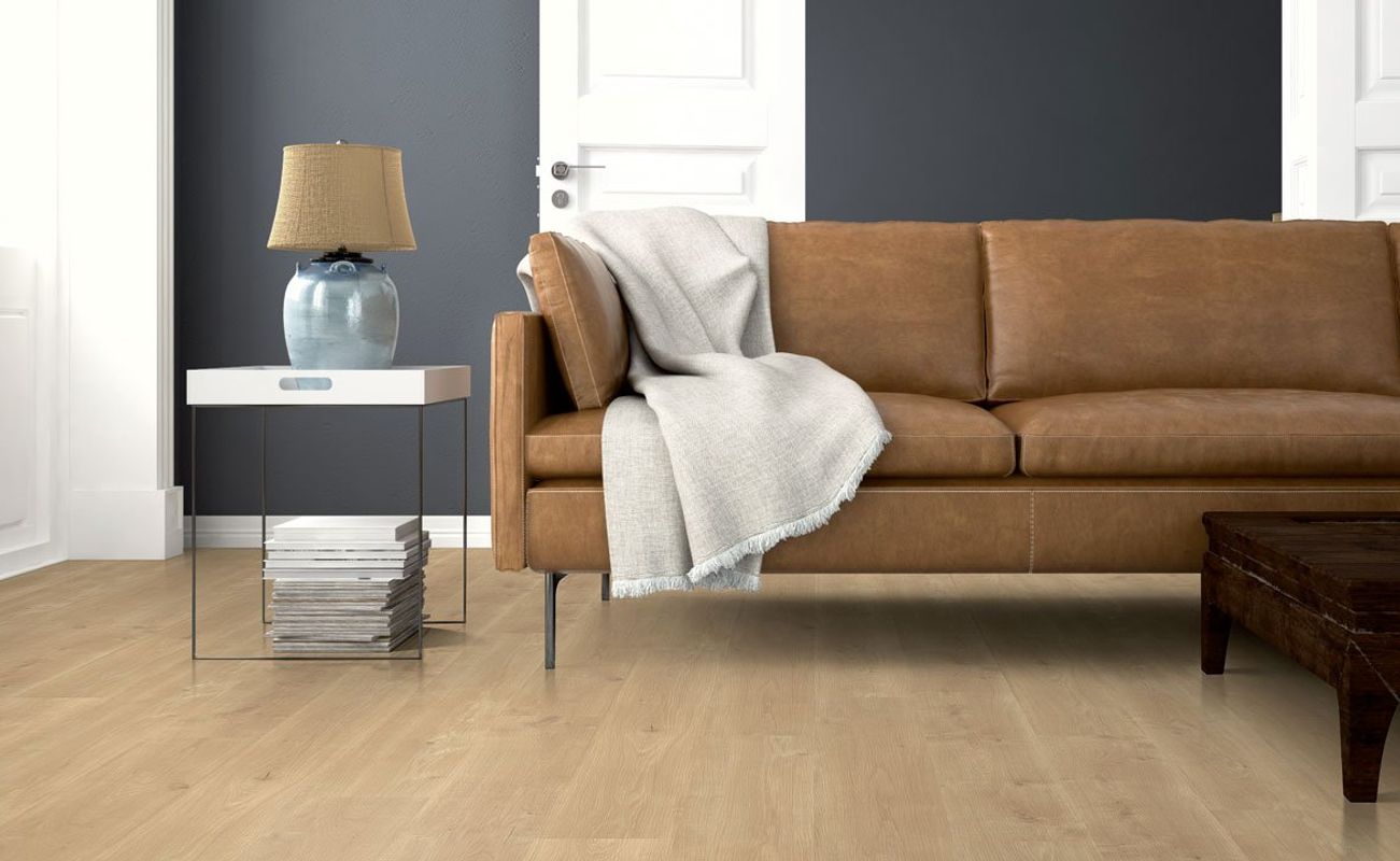 Ein Wohnzimmer mit einem braunen Sofa, einem Tisch und einer Lampe. Der Boden ist hell, die Wände sind dunkelgrau.