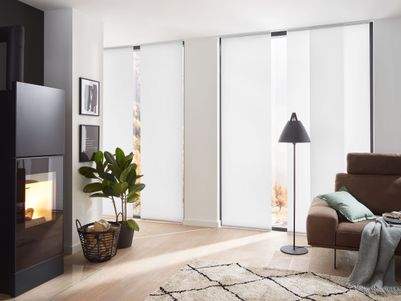 Moderne Wohnzimmereinrichtung mit einem Kamin, einer Stehlampe, einem Sofa und Pflanzen. Helle, lichtdurchlässige Vorhänge lassen Tageslicht herein.